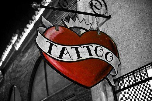 Tatuador profissional trabalhando em um estúdio moderno com equipamentos de alta qualidade, usando luvas e com braços cobertos por tatuagens coloridas